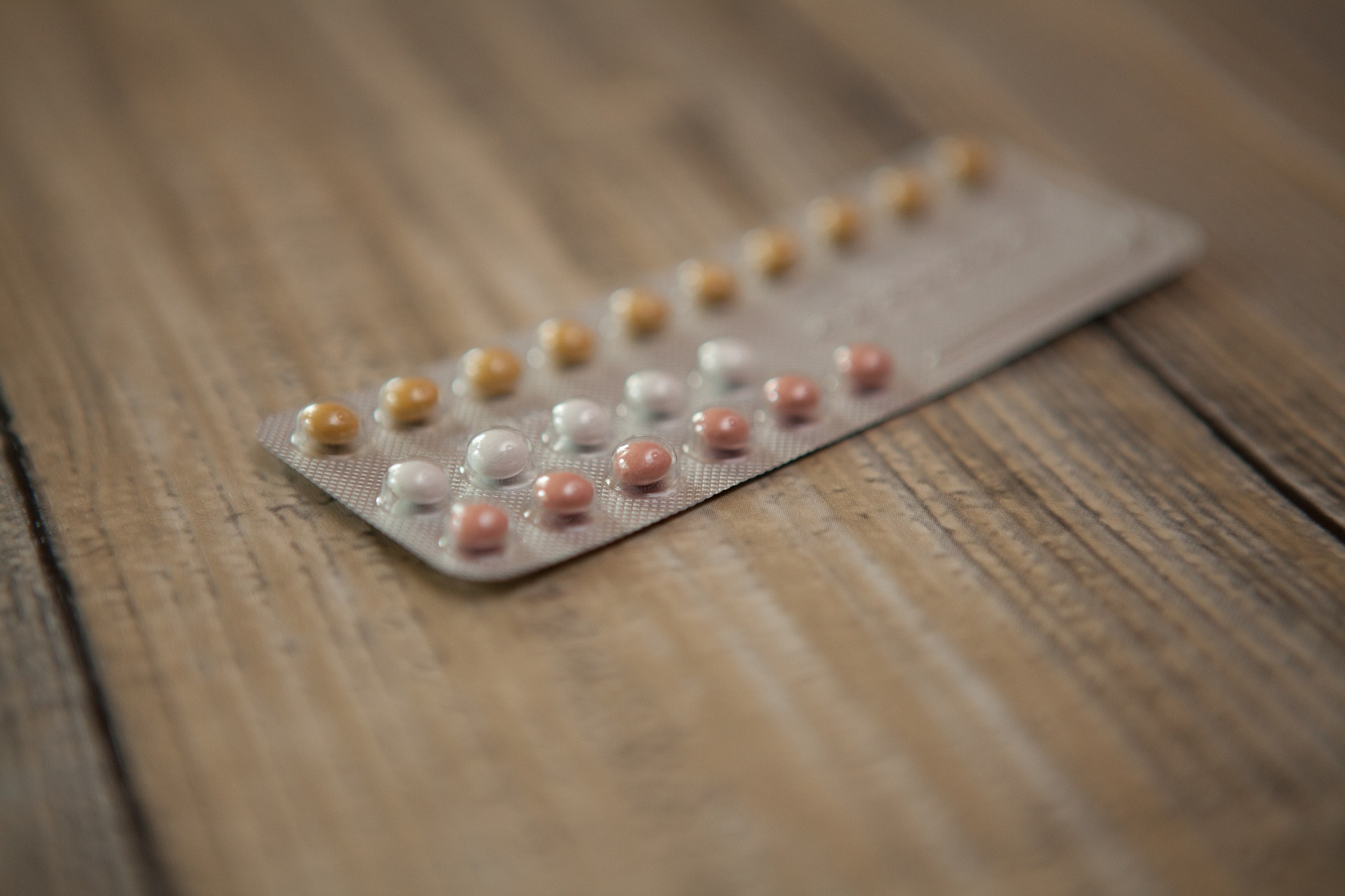 A blister pack of multicoloured contraceptive pills rests on a wooden surface. The pills are arranged in rows of orange, white, and pink tablets. Could the mini-pill be right for you? Explore your options and find what fits your needs.