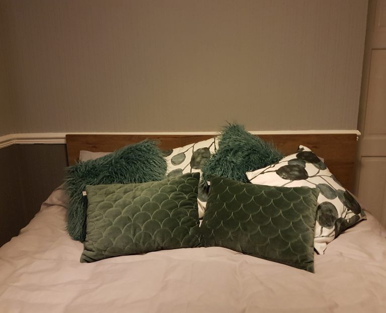 King Size Bed with grey duvet covers and lots of cushions that are green and white in colour, making it look cosy and adding to the Hygge feeling