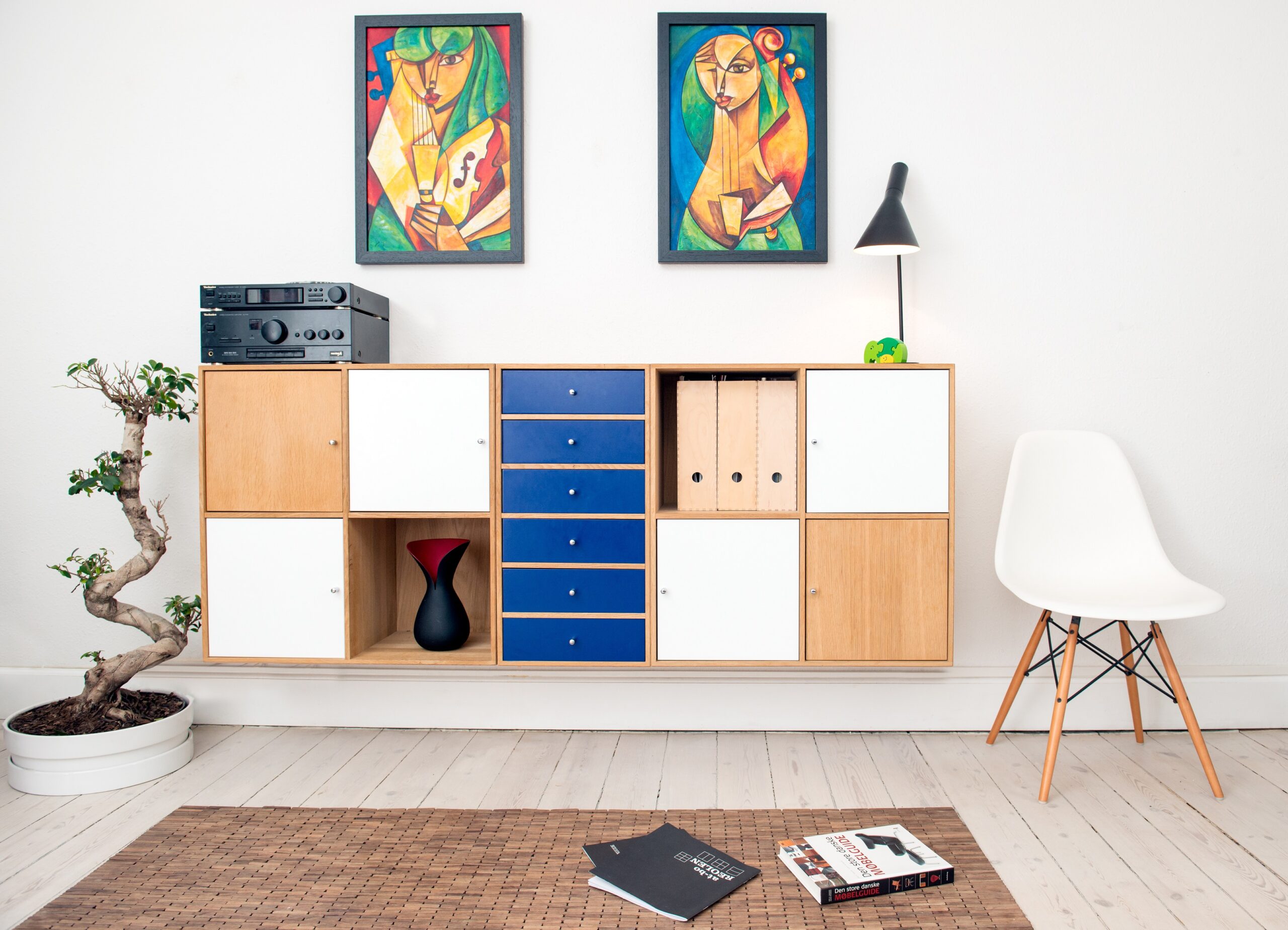 living room sideboard, skirting board, coffee table, lamp, plant and white chair. There are two pictures on the wall - each full of colour