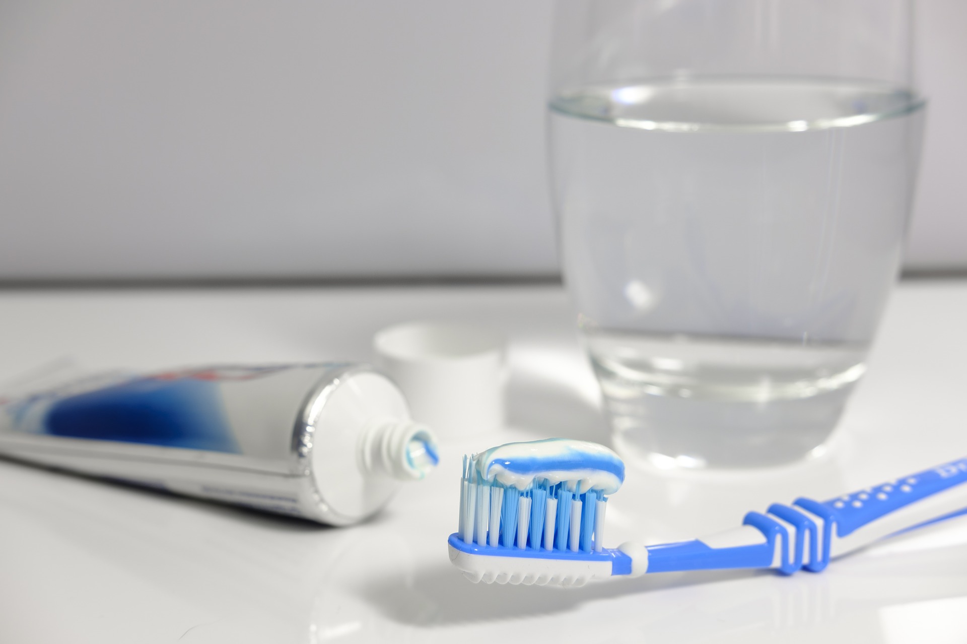 opened tube of toothpaste, a toothbrush with toothpaste on it and a glass of water - items needed for good oral health