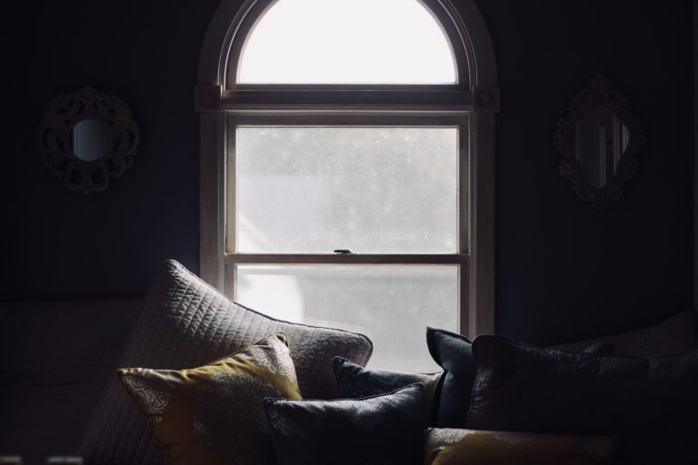 A cosy home scene - a sofa with lots of soft cushions in front of a window