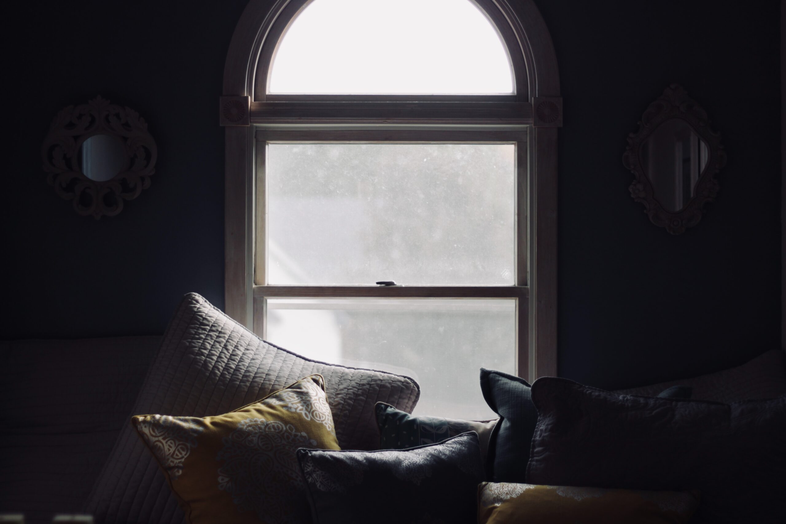A cosy home scene - a sofa with lots of soft cushions in front of a window