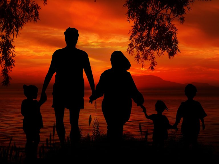 A family of five holding hands stood on a bank over looking a lake at sunset
