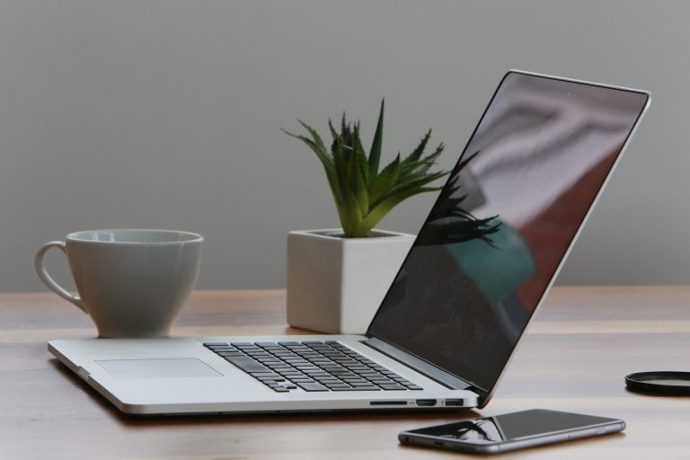 clutter free work area consisting of a laptop, a mobile phone, plant and cup of coffee