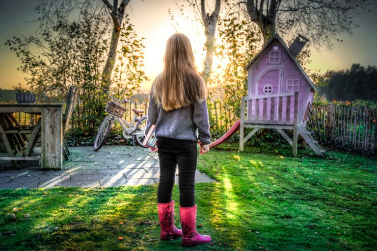 a little girl in a garden near a pink Wendy house and bicycle