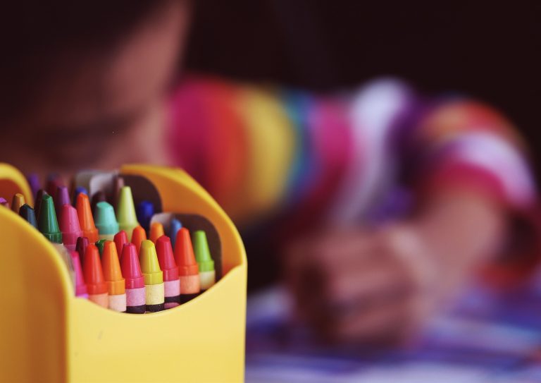 A box of crayons sat in front of a child colouring in