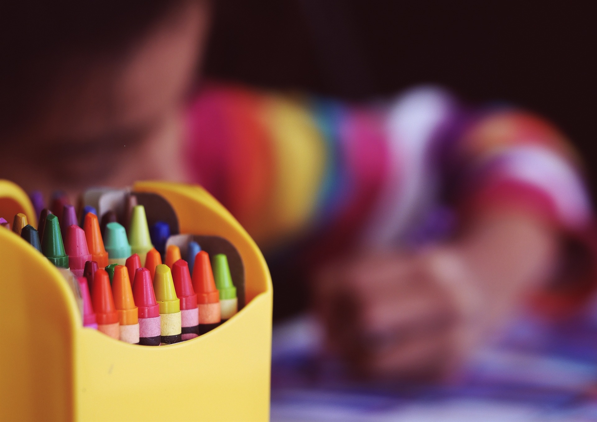 A box of crayons sat in front of a child colouring in