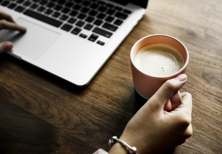 A woman sat to a table with a laptop and a cup of coffee