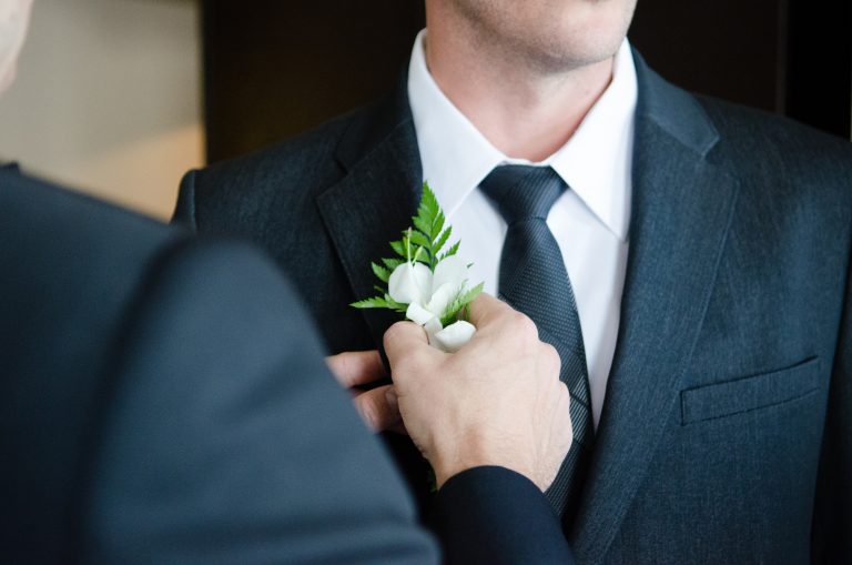 A groom having a white button hole flower added to his black suit on his wedding day
