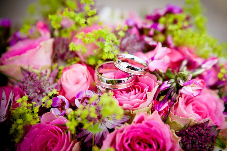 A brightly coloured wedding bouquet with wedding rings sat on top