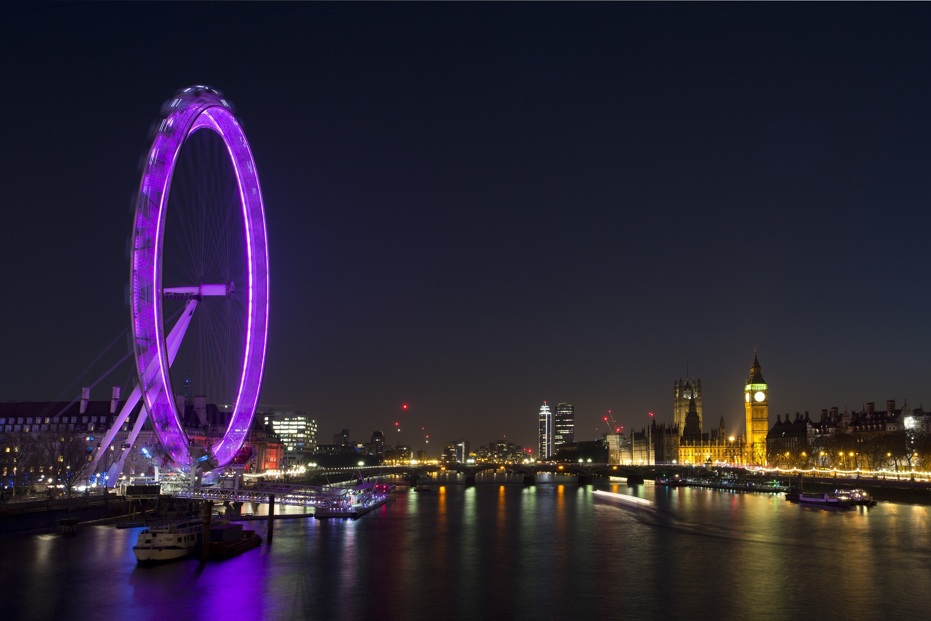 London skyline at night. Houses of Parliament is lit up across the river Thames and the London Eye is lit up purple