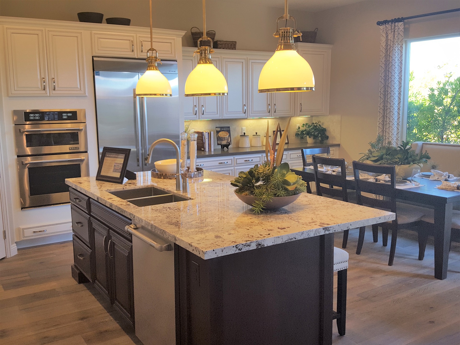 three round lights hanging over a kitchen that has an island consisting of a double sink and tap. You can see the dining table in the background and a double oven too