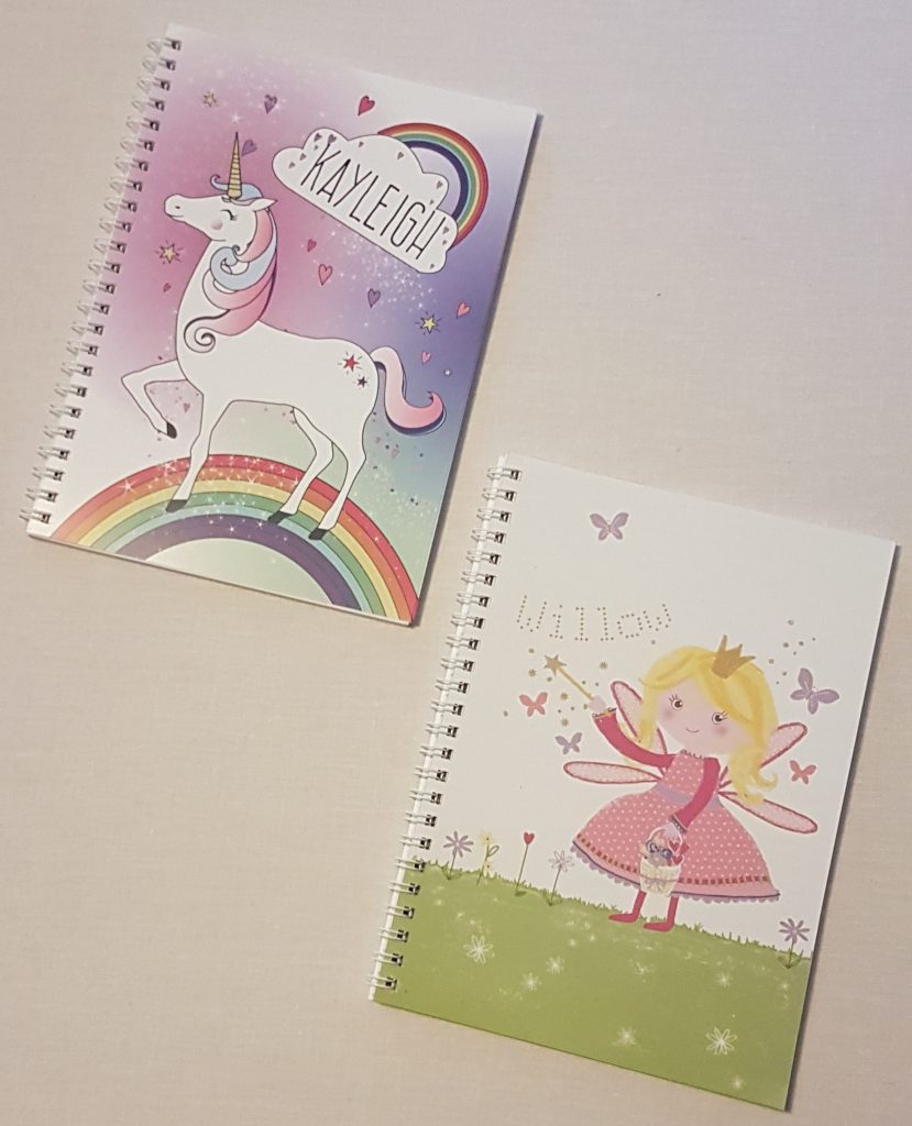 Two spiral notebooks: one with a unicorn and rainbow design labelled "KAYLEIGH," and one with a fairy in a pink dress labelled "WILLOW," perfect for back to school 2018, both displayed on a light surface.