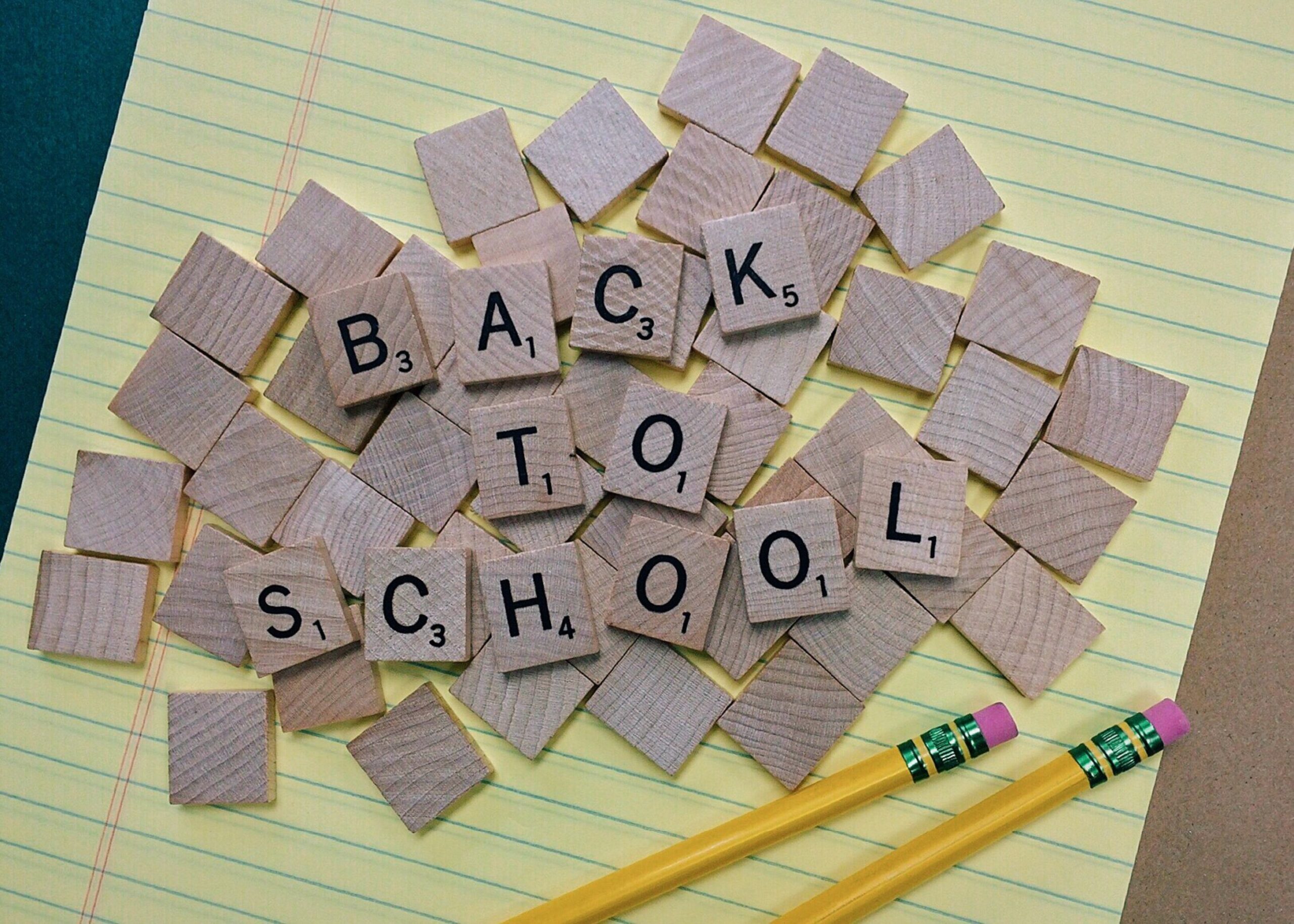 Back to school written in scrabble pieces on top of a yellow piece of paper