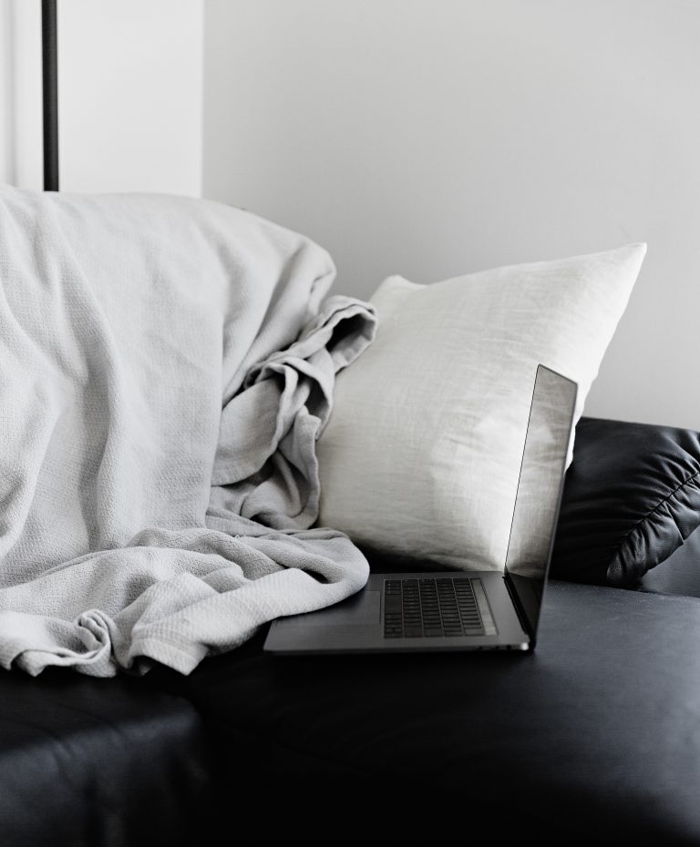 laptop on a sofa with a cushion and throw nearby
