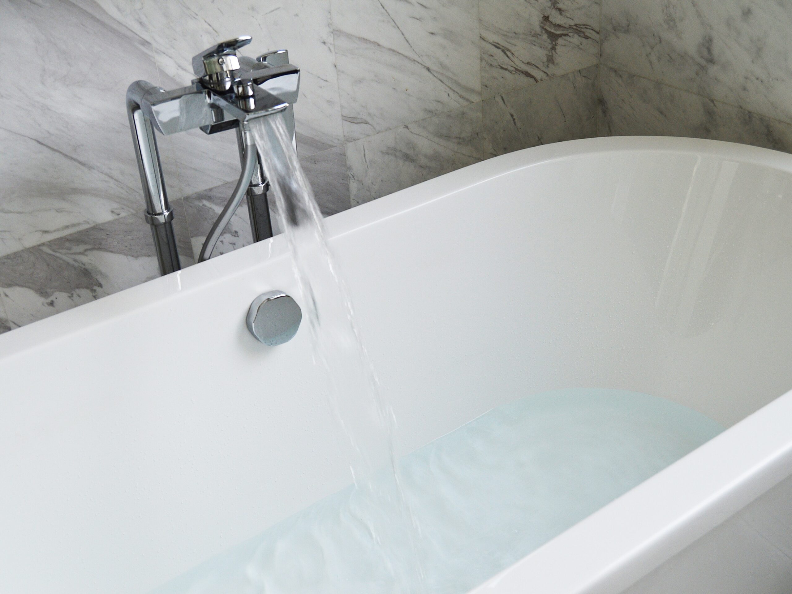 water running into an oval shaped bath - the room has marble effect tiles