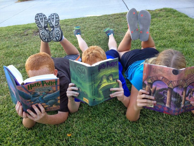 three children laid on the grass reading Harry Potter