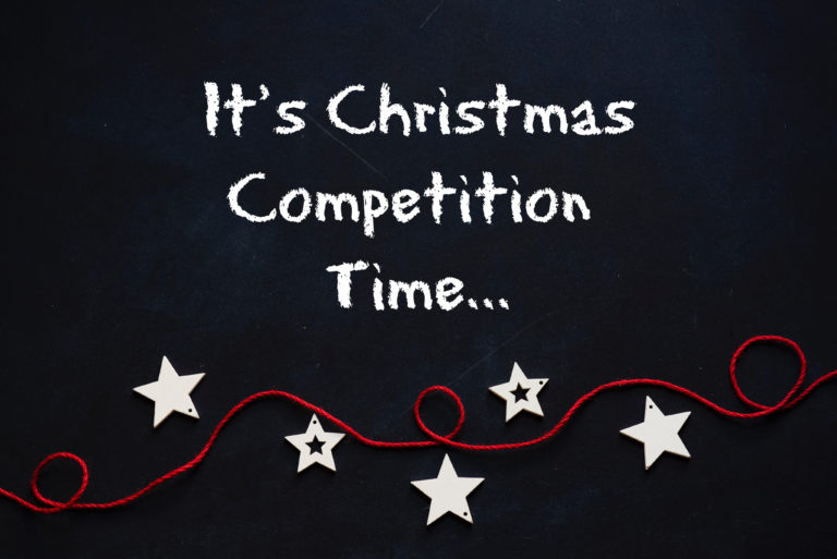 Blackboard with the text "It's Christmas Competition Time..." above a red string decorated with white star ornaments, inviting you to join the festive Christmas Cadbury competition.