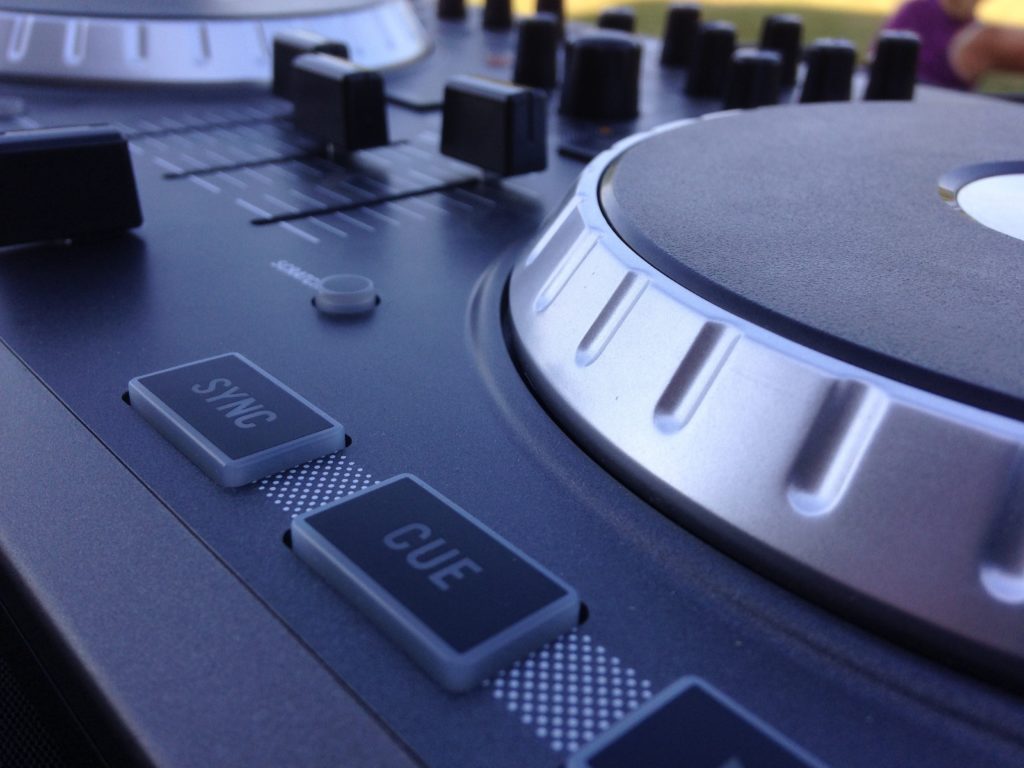 Close-up of a DJ controller at a wedding in Michigan, highlighting the jog wheel, faders, and "SYNC" and "CUE" buttons, with a softly blurred background.