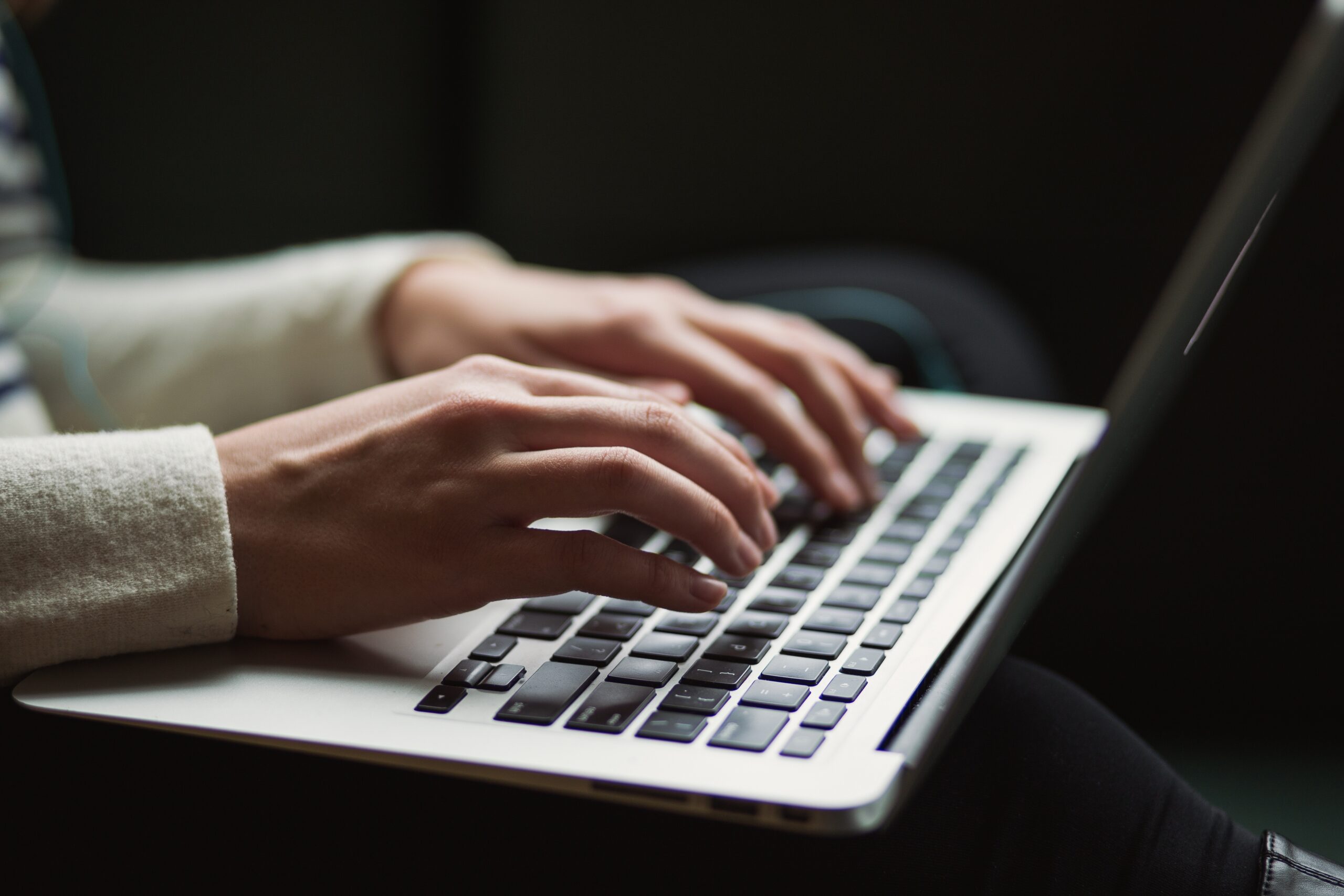 Close-up of a person’s hands typing on a laptop keyboard, possibly using a VPN for secure browsing, with the screen slightly out of focus and the background darkened.