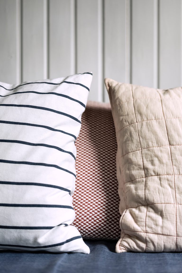 Three pillows on a sofa—striped, geometric, and quilted—against a white panelled wall, offering easy ways to update your child's bedroom with playful patterns and cosy textures.