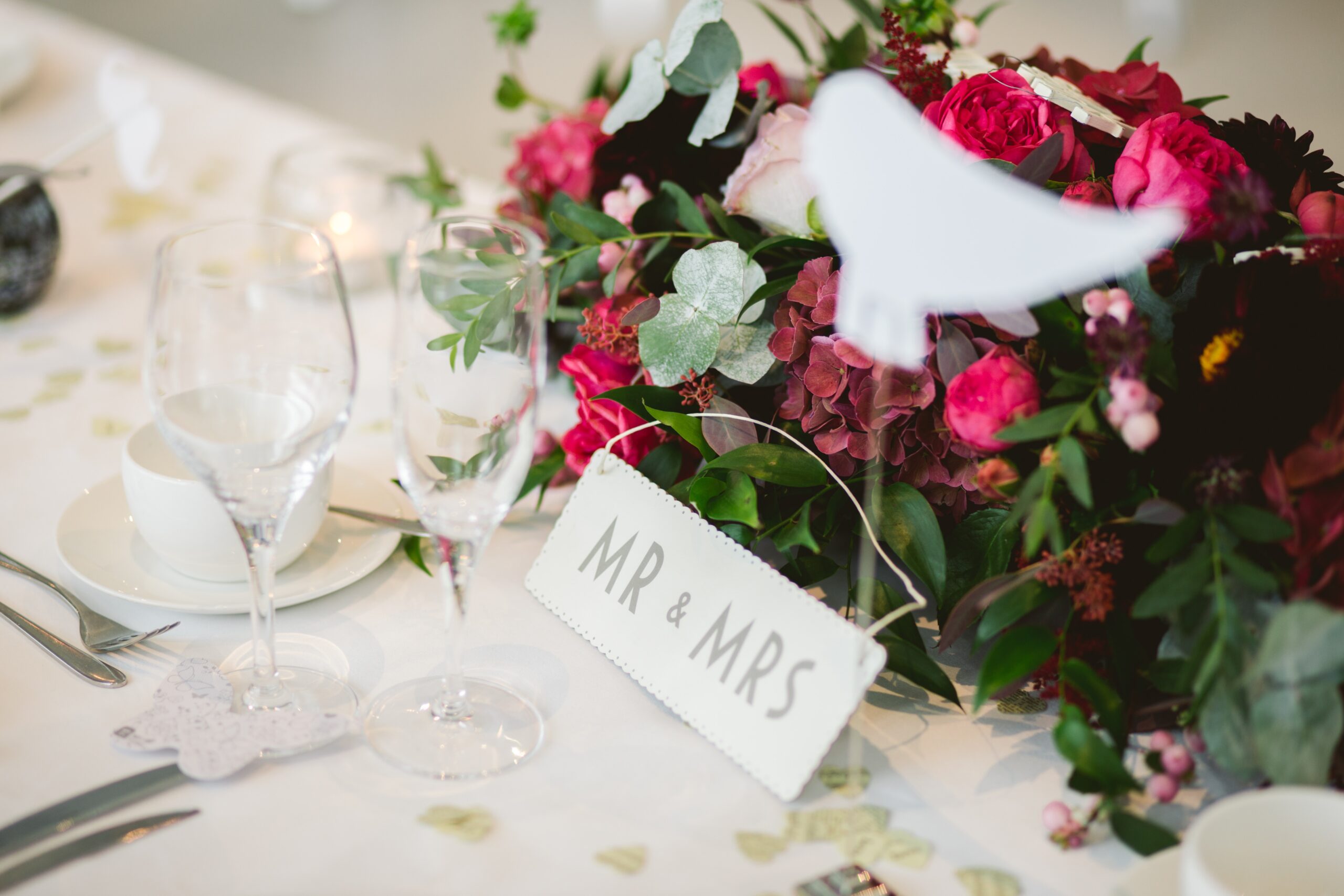 wedding table set up - bridal bouquet, wine glasses and a his and hers name card