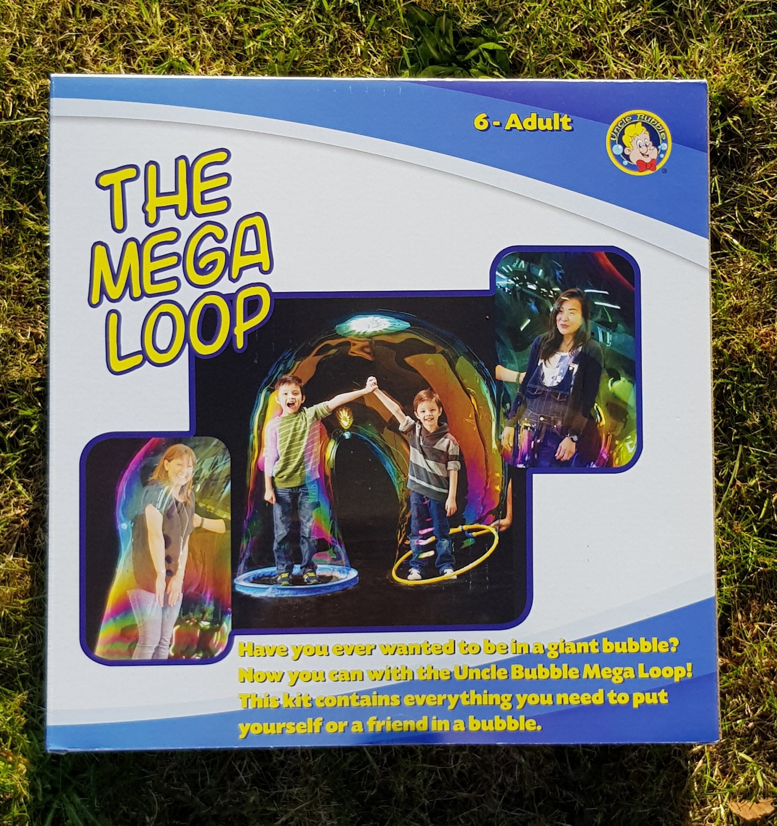 A box for "The Mega Loop" Giant Bubble Making Kit, showing three children each standing inside a giant bubble. The packaging is white with blue and yellow text and graphics, suitable for ages 6 to adult.