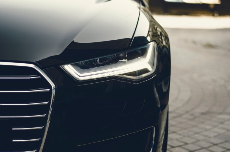 Close-up of the front left headlamp and grille of a sleek black car, showing modern LED lights and reflecting the outdoor environment—a perfect choice for anyone selling a private number plate to complement its stunning style.