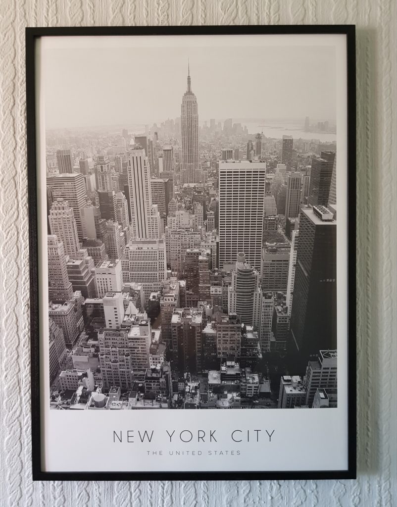 Black and white framed photograph from Desenio of New York City’s skyline with the Empire State Building at the centre, hanging on a patterned wall. The text at the bottom reads "NEW YORK CITY THE UNITED STATES.