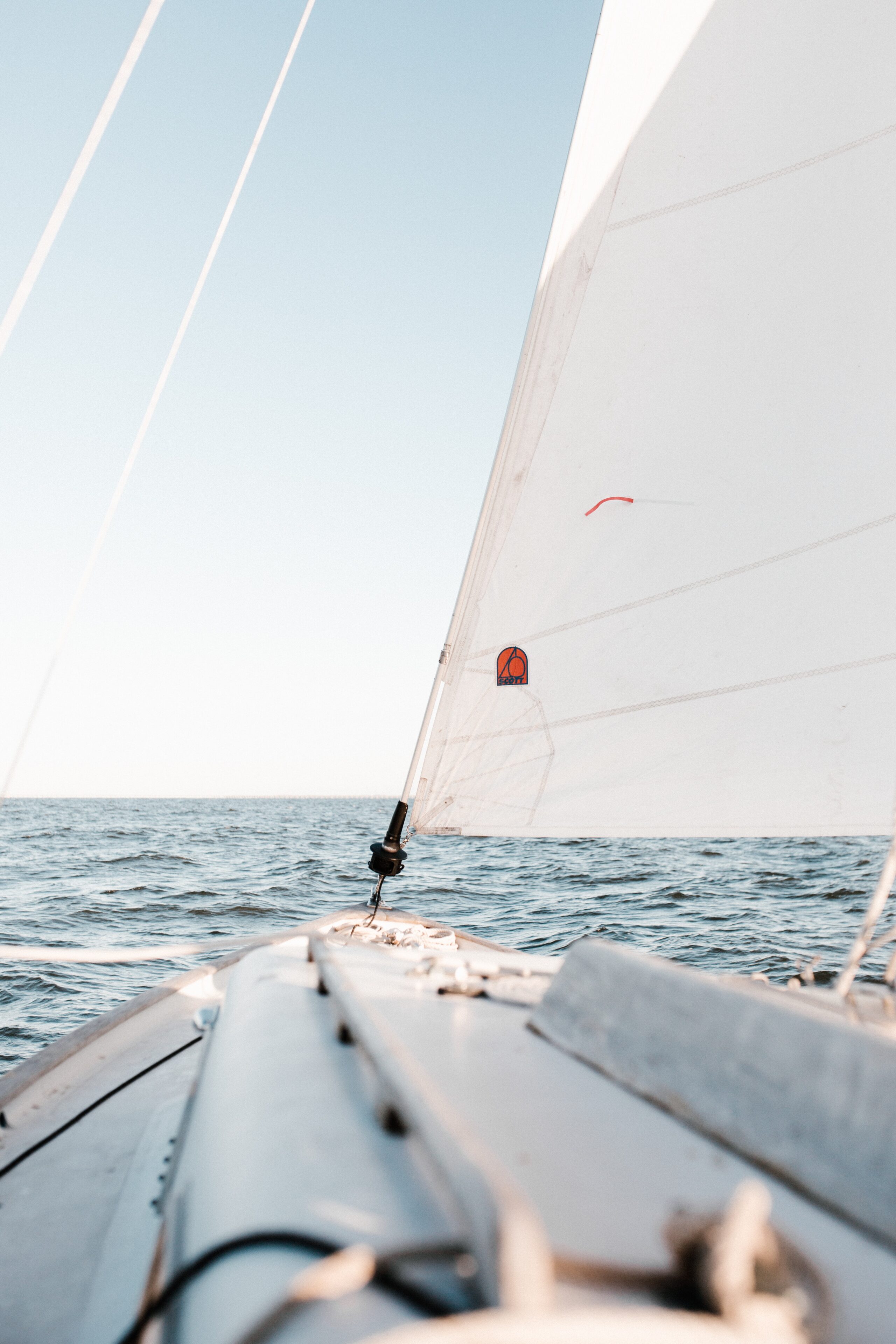 View from a sailing boat looking forward, showing the deck and white sail against a clear blue sky and calm sea water—evoking the peacefulness of sailing off the coast of Morocco.