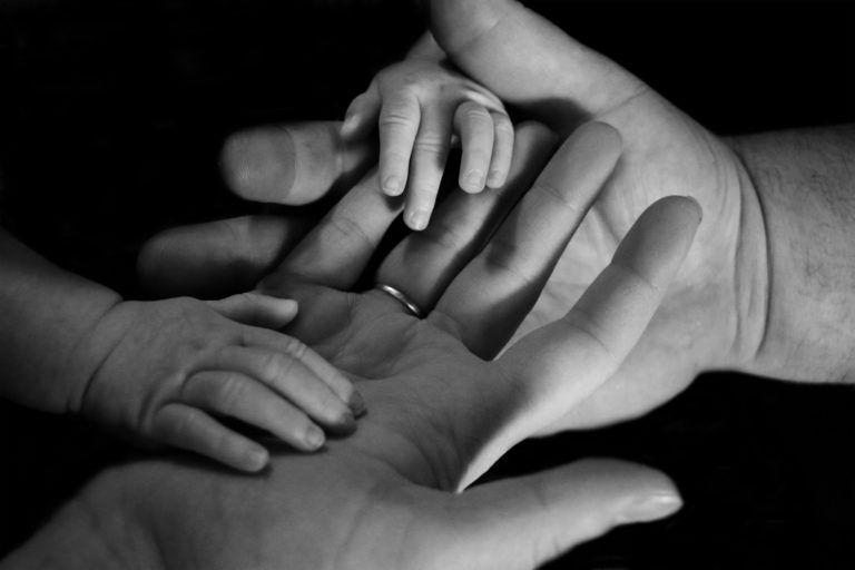A black and white photo shows an adult’s, a child’s, and a baby’s hands gently layered together, symbolising family connection, care, and the legacy built through thoughtful family wealth planning.
