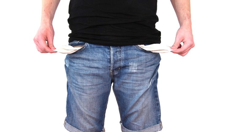 A person wearing a black shirt and blue jeans is standing with both hands pulling out empty pockets, suggesting a lack of control over your finances.