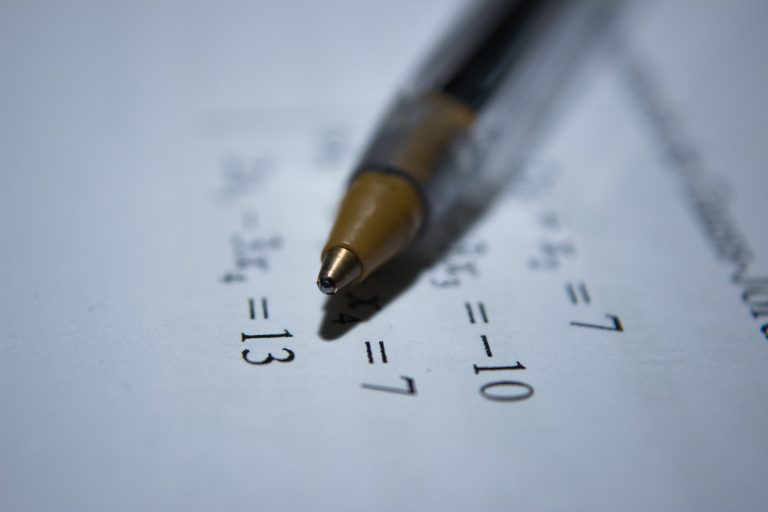 A close-up of a pen pointing at mathematical equations printed on white paper, with numbers and equal signs clearly visible—perfect for a teach to one learning environment.