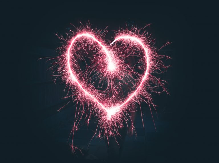 A glowing pink heart shape, reminiscent of the products I'm loving, is drawn in the air with a sparkler against a dark background, creating a bright, sparkling outline.