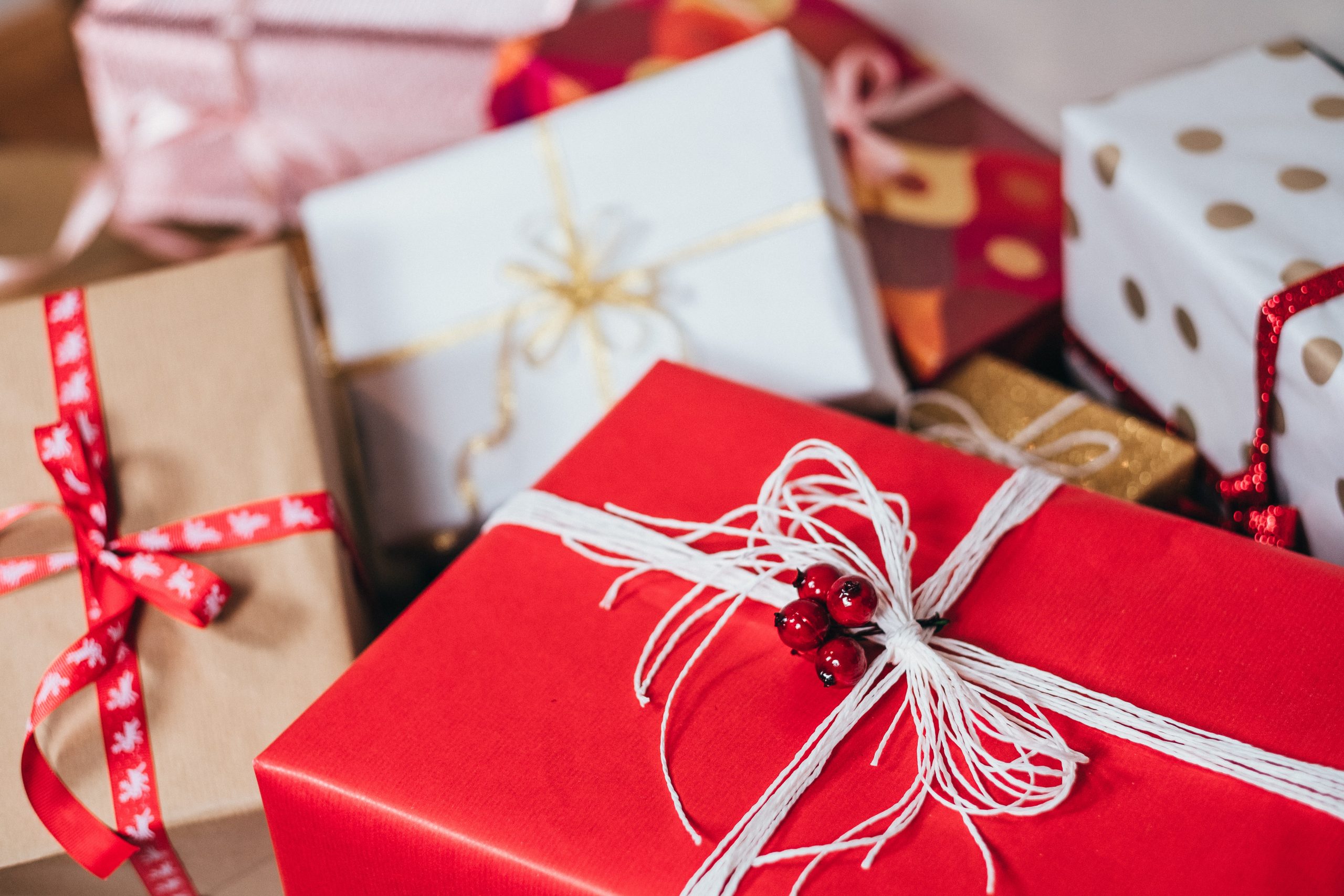 A close-up of several wrapped Christmas presents for adults in colourful papers—red, white, gold, and patterned—tied with decorative ribbons and string, all arranged in a festive display.