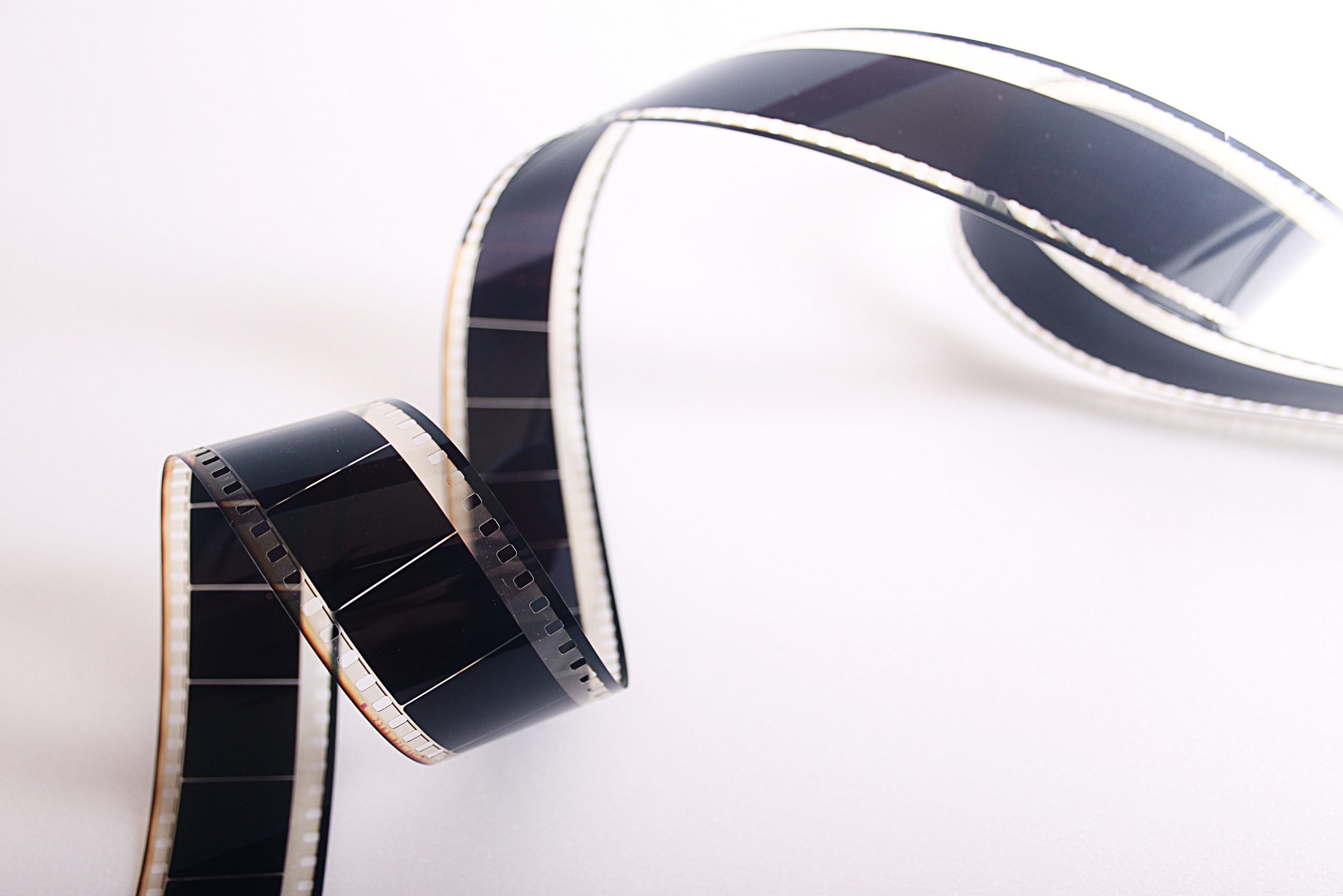 A close-up of a curled strip of 35mm film negative, featuring visible frames and perforated edges, set against a white background—perfect inspiration for any cinema gift card competition.