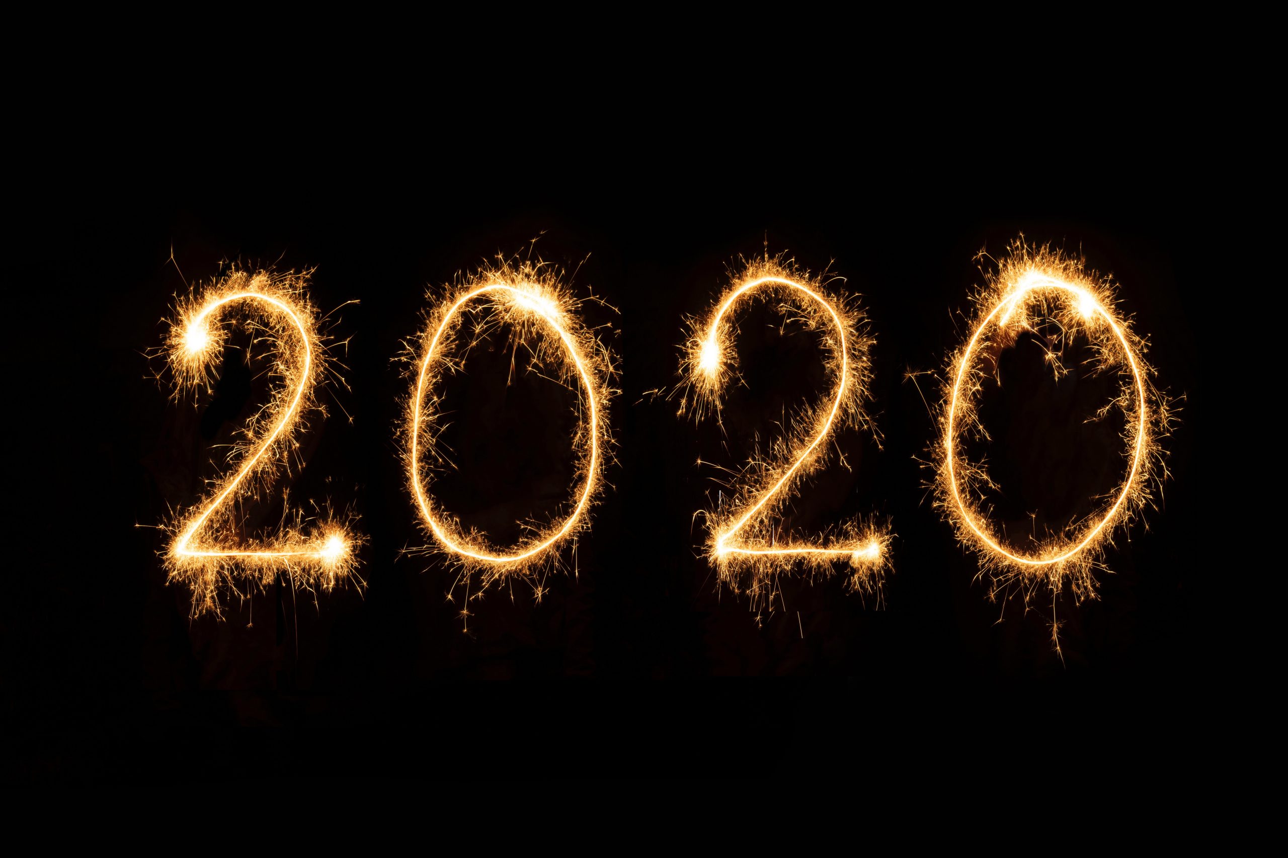 The year "2020" is written in glowing golden sparkler light against a black background, capturing a festive atmosphere that says Hello 2020 and Goodbye 2019.