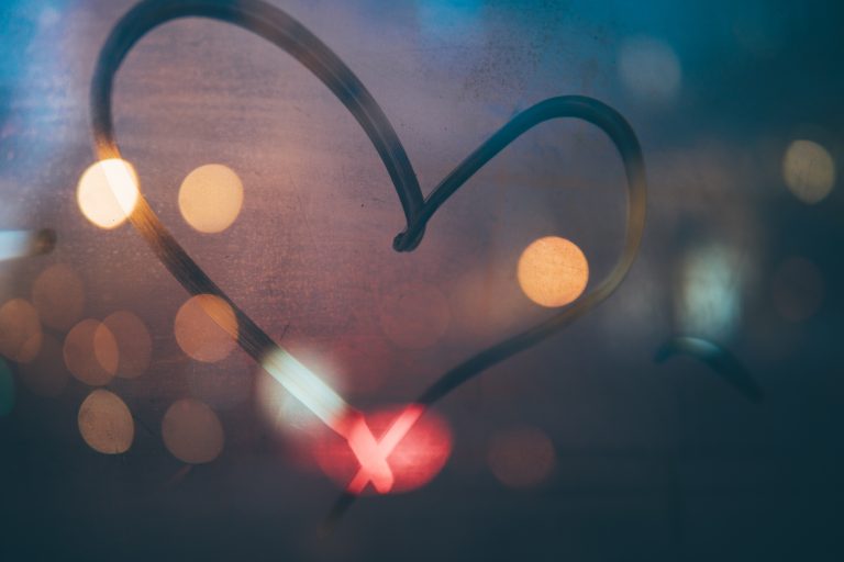 A heart shape is drawn on a misty window with colourful city lights blurred in the background, creating a warm, dreamy atmosphere—perfect inspiration for homemade Valentine’s Day gift ideas.