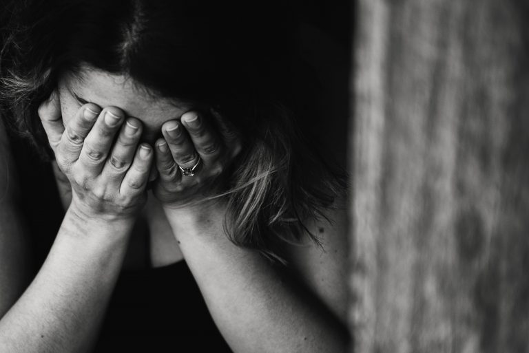 A person sits with their head in their hands, covering their face, appearing distressed or upset. The black and white image emphasises a sombre mood, subtly highlighting the search for relief such as through cannabidiol.