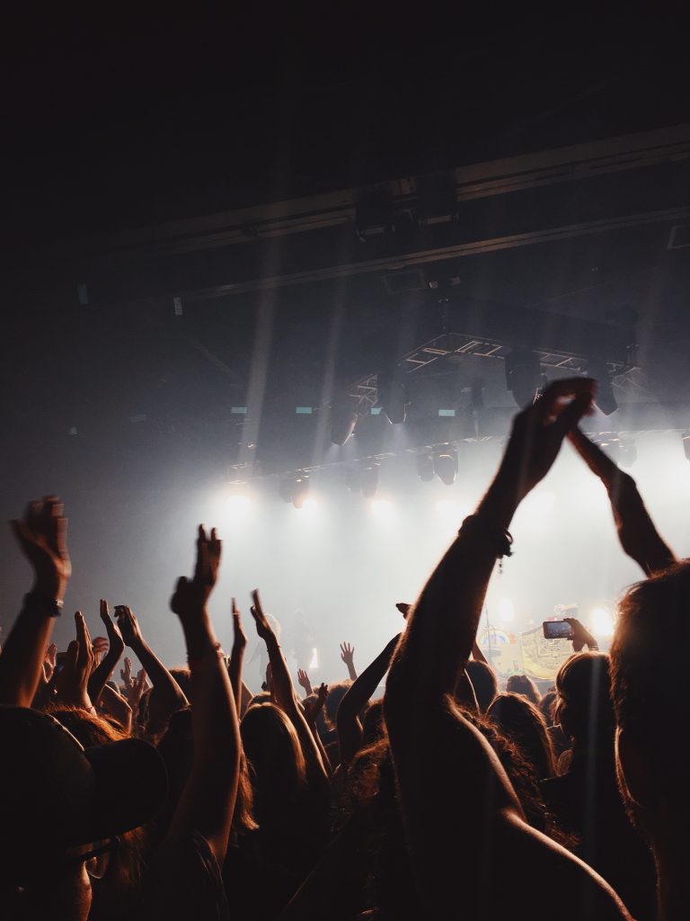 A large crowd at a concert in Manchester raises their hands in the air under bright stage lights, creating a lively and energetic atmosphere—one of the top things to do in Manchester for music lovers.