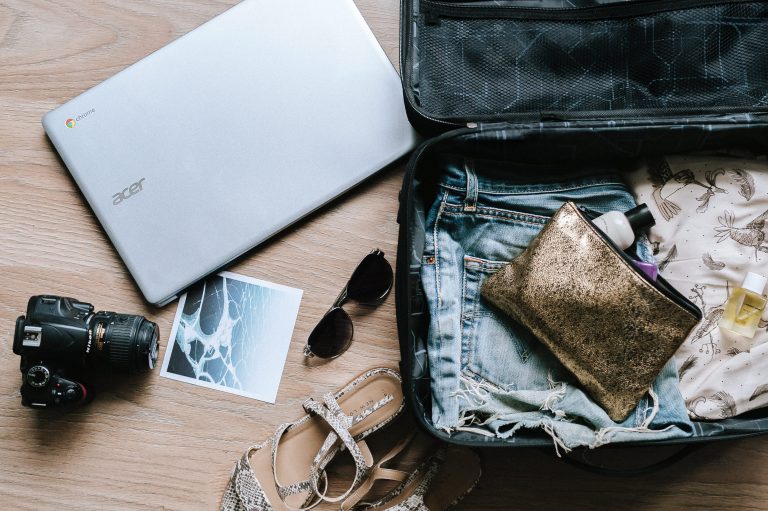 an open suitcase with clothes and a handbag sat inside it. A laptop and camera sat next to it