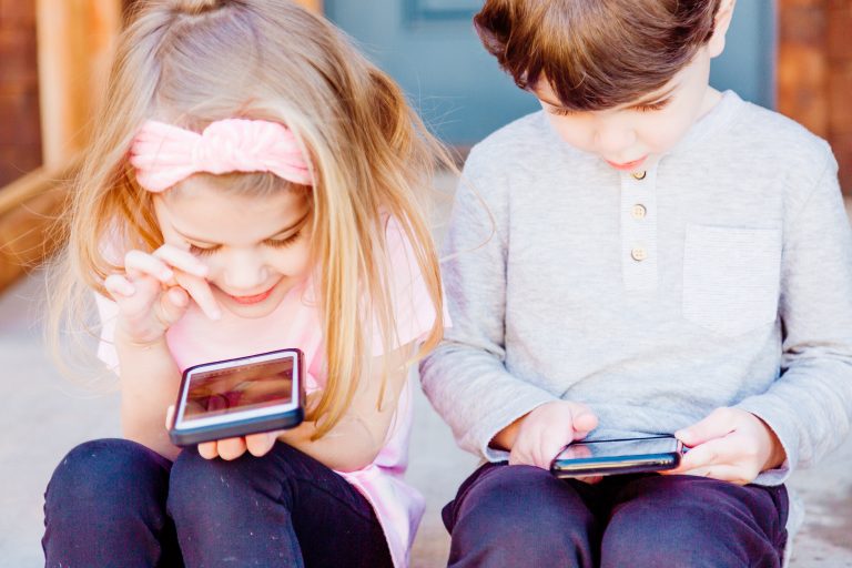 two children sat playing with a smartphone each