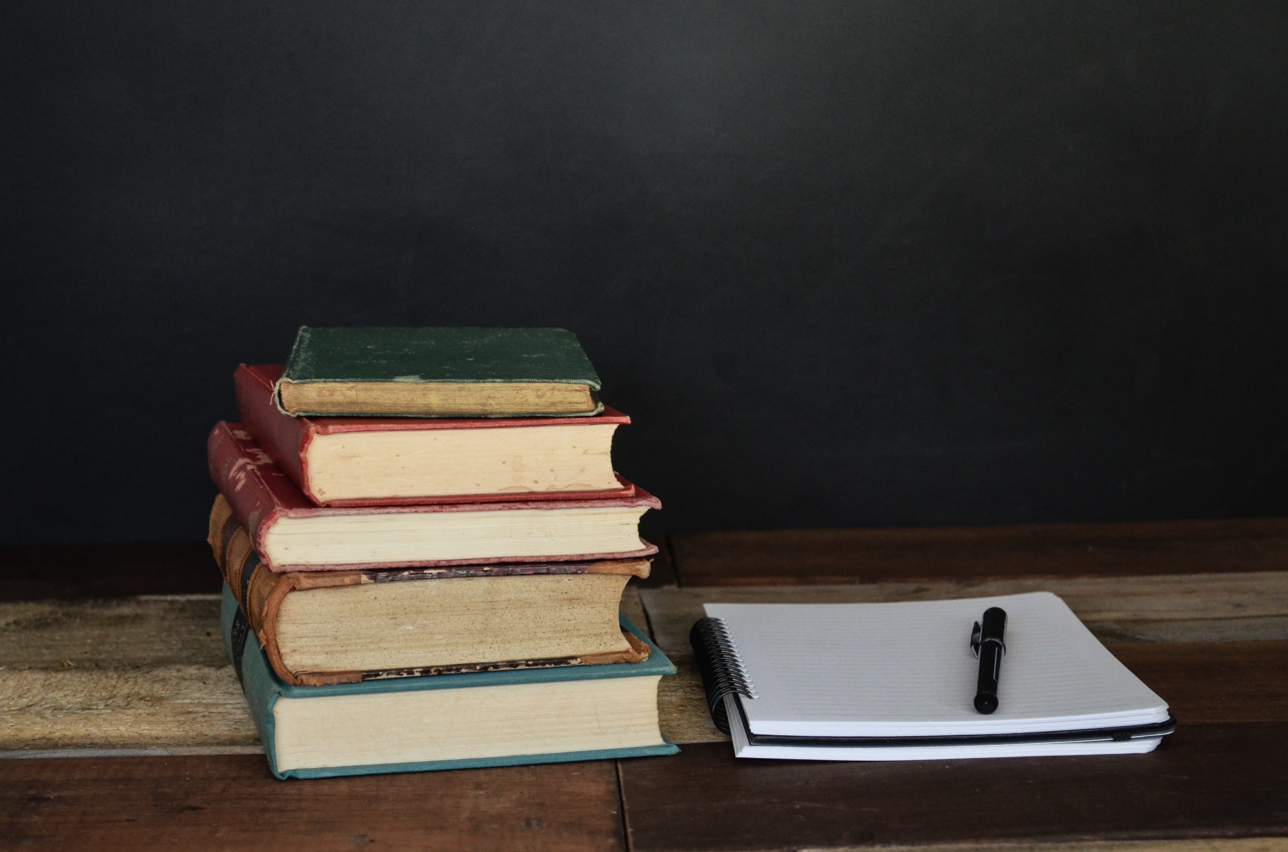 text books and a pad of paper sat on a desk in front of a blackboard