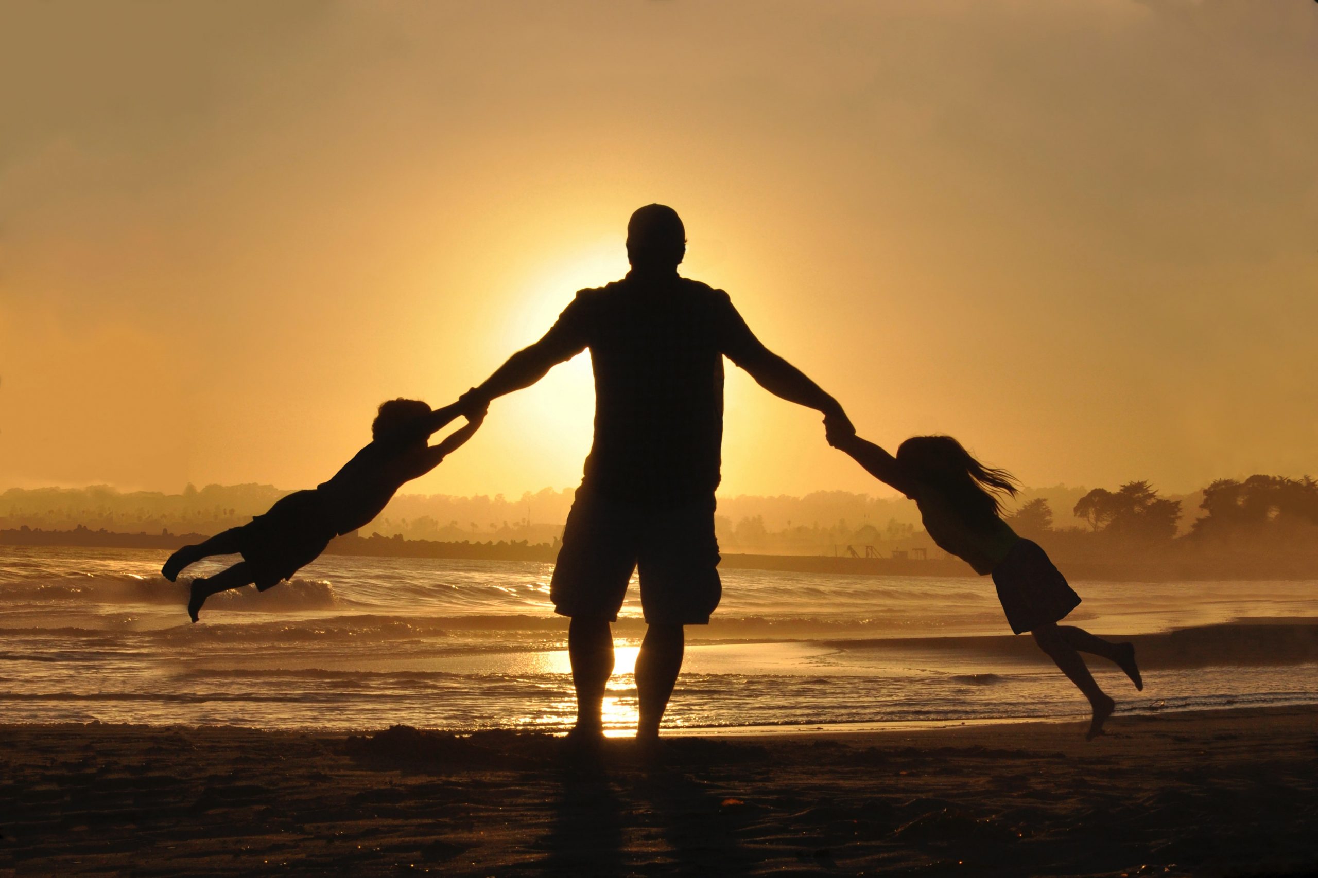 A man swinging two children round on the beach at sunset