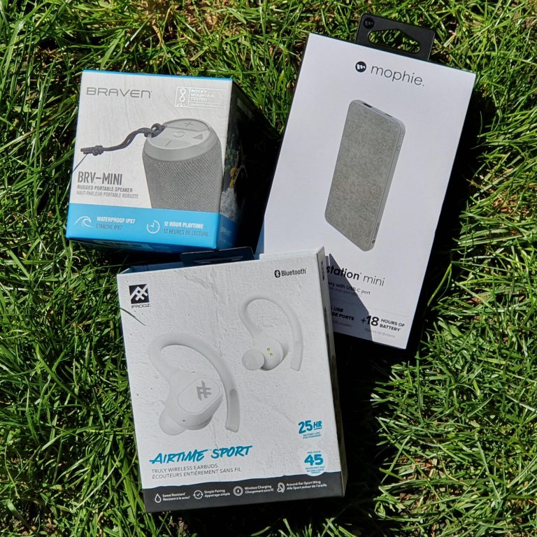 Three electronics boxes lying on grass: a Braven BRV-Mini Bluetooth speaker, Mophie Powerstation Mini portable charger, and Altec Lansing Airtime Sport Bluetooth earbuds—perfect work from home gadgets for productivity and convenience.