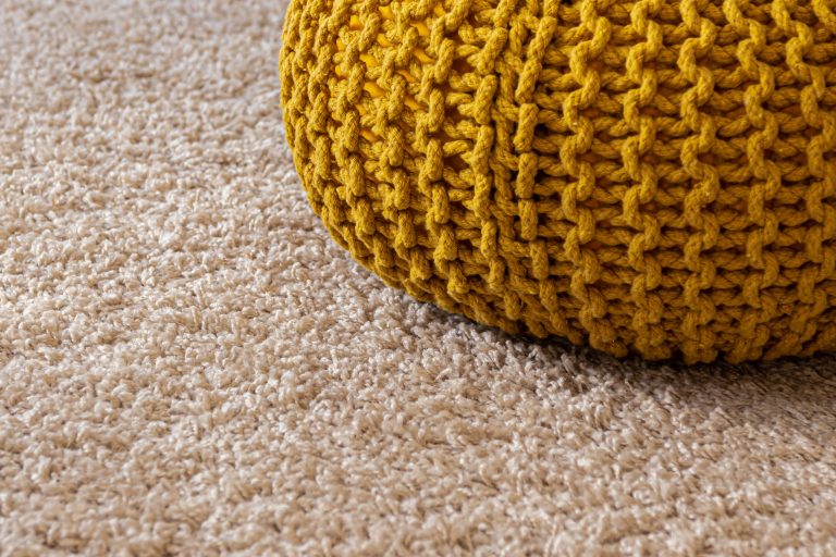 a yellow knitted cushion on a carpeted floor