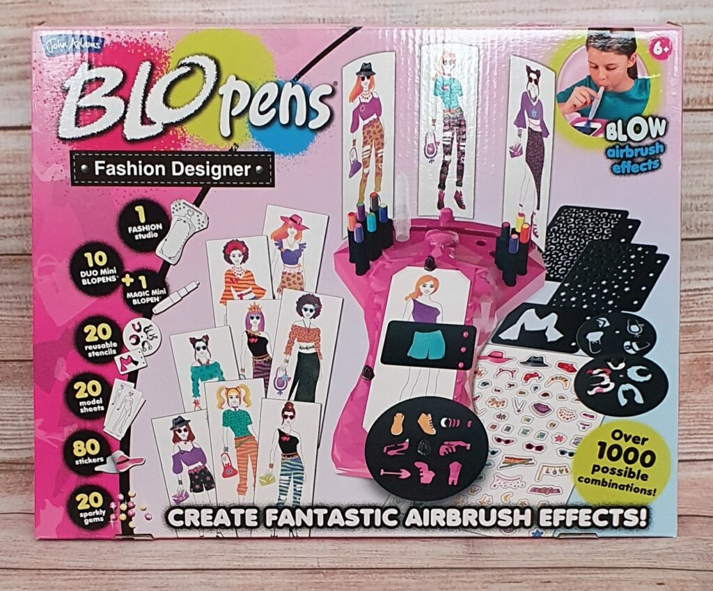 The image shows the BLOpens Fashion Designer kit box, a creative fashion toy. The packaging features drawings of fashion models, clothing, accessories, and airbrush art tools. It advertises “Over 1000 possible combinations!” and is designed for ages 6+.
