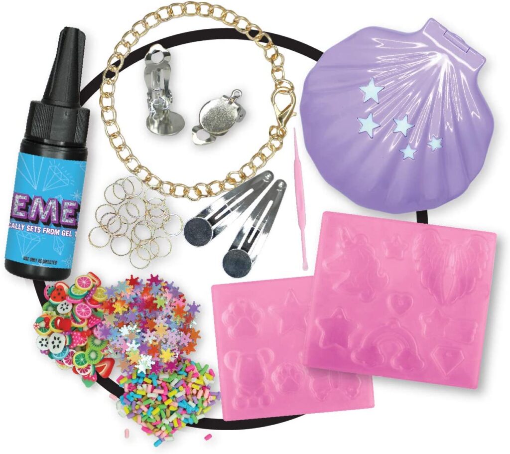 A resin craft kit with fashion toys flair—includes silicone moulds, glue, a gold chain, metal charms, hair clips, tweezers, jump rings, colourful sprinkles, fruit slices, star confetti, and a purple shell-shaped case.