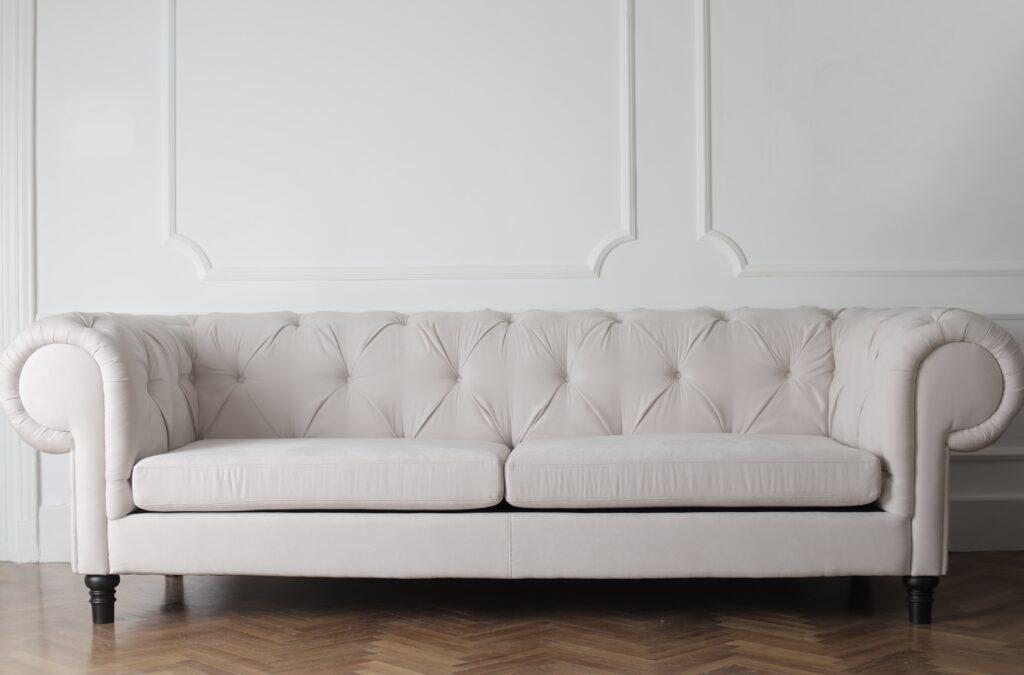 A white sofa sat in front of a white paneled wall on a dark brown wooden parquet floor