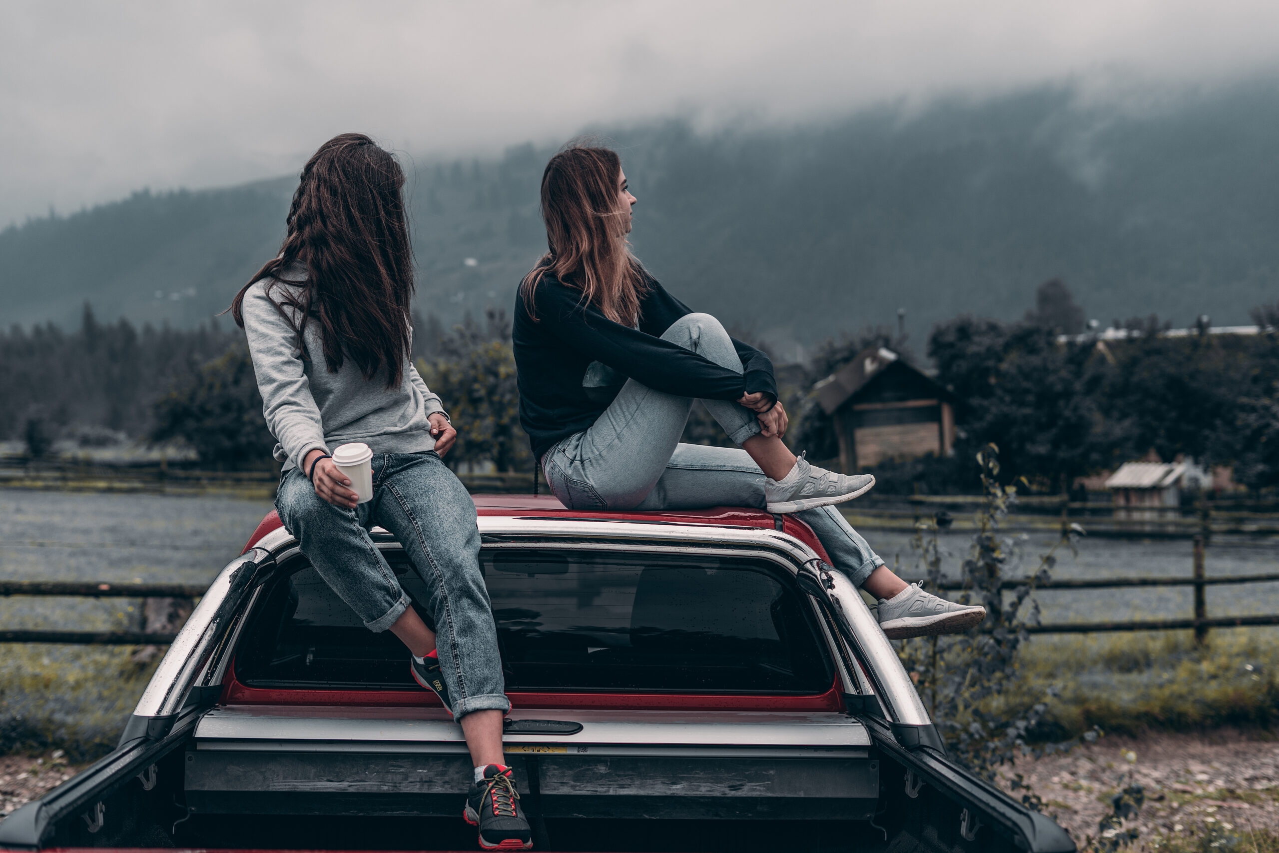 Two teenage women sat on the top of a car